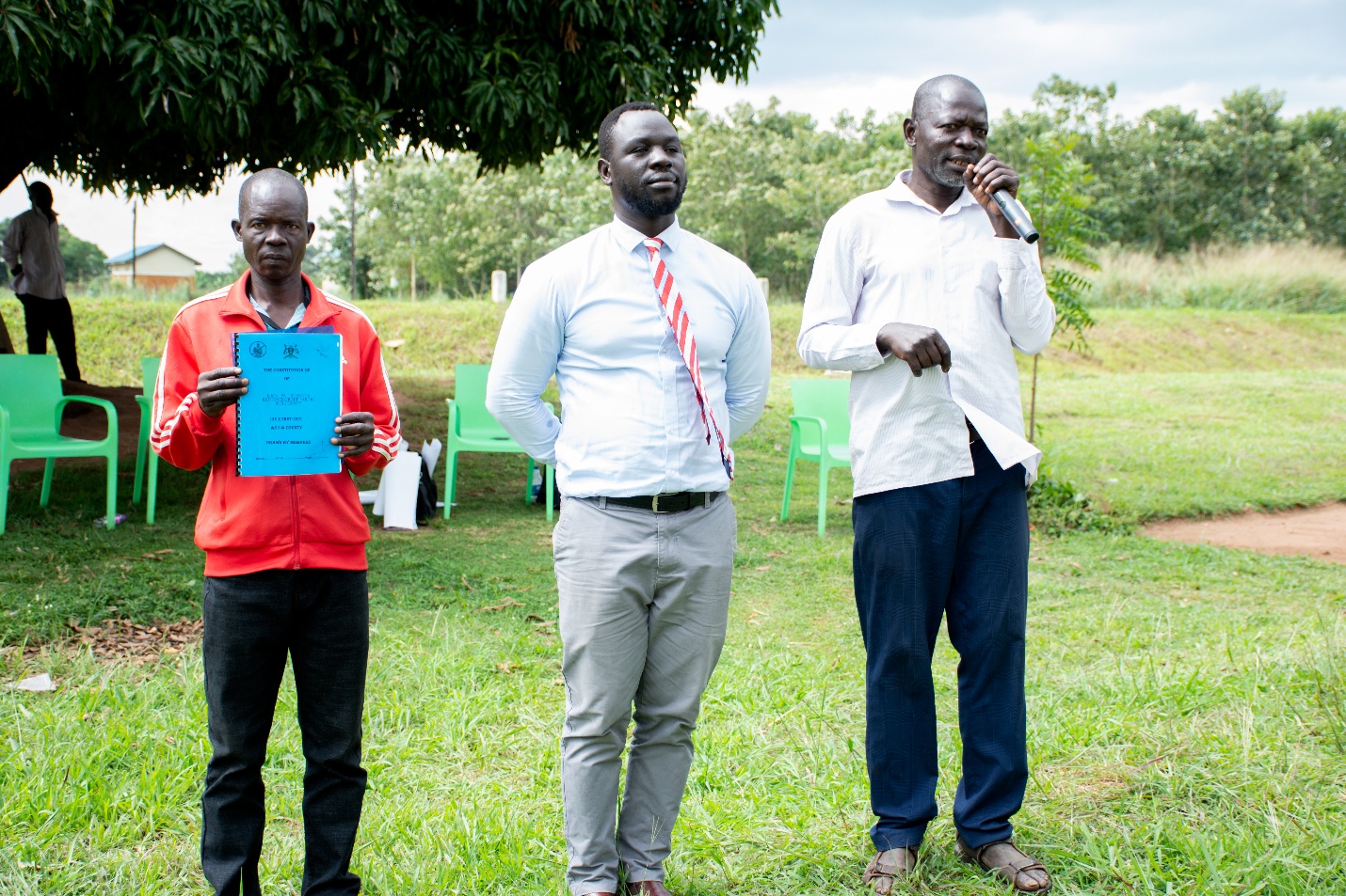 A group of men standing in a grass field holding a microphone and a paper AI-generated content may be incorrect.